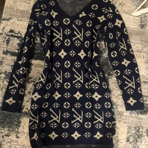 Mönstrad stickad klänning - Snygg marinblå stickad klänning med ett unikt mönster i beige. Klänningen har en v-ringad hals och långa ärmar, perfekt för kyligare dagar. Den är både stilren och bekväm, vilket gör den till ett mångsidigt tillskott i garderoben.