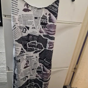 Svartvit klänning med tidningsmönster - Trendig svartvit klänning med unikt tidningsmönster. Klänningen är ärmlös och har en tight passform, perfekt för en modern look. Materialet är mjukt och bekvämt, vilket gör den idealisk för både vardag och speciella tillfällen.