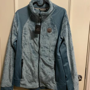 Ny! Isblå supermjuk pile fleecejacka från JH Collection - Säljer en mjuk och bekväm isblå fleecejacka från JH Collection. Jackan har en dragkedja framtill och en hög krage för extra värme. Perfekt för kyliga dagar. 