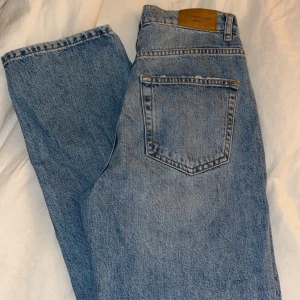 Blå jeans från Gina tricot  - Snygga blå jeans från Gina tricot med klassisk femficksdesign och knappgylf. De har en normal passform och är perfekta för en avslappnad stil. Märkesdetaljer på knappen och etiketten ger en autentisk touch.