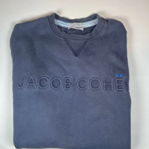 Mörkblå sweatshirt från Jacob Cohën - Säljer en stilren mörkblå sweatshirt från Jacob Cohën med broderad logotyp på bröstet. Tröjan har rund hals och ribbade muddar vid ärmslut och nederkant. Perfekt för en avslappnad stil. Pris kan diskuteras 