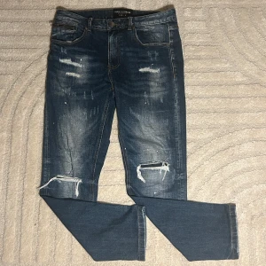 Blå jeans från Supply & Demand - Snygga blå jeans från Supply & Demand med slitna detaljer och en cool, avslappnad look. De har en klassisk femficksdesign och knappgylf. Perfekta för en trendig stil.