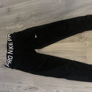 Träningstights från Nike - Snygga svarta leggings från Nike med vit logga och text på midjan. Perfekta för träning med en tight passform och elastisk midja för extra komfort.