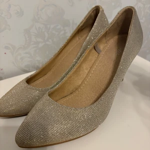 Glittriga klackar  - Snygga glittriga pumps i beige med spetsig tå och klack. Perfekta för att lägga till lite glamour till din outfit. De har en elegant design som passar till många tillfällen.