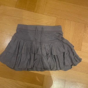 Grå glittrig kjol med volanger - Säljer en söt grå kjol med glittrigt tyg och volanger. Kjolen har en kort längd och låg midja. Perfekt för att lägga till lite glitter i vardagen! Eller på fest.