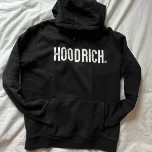Svart hoodie från Hoodrich - Säljer en svart hoodie från Hoodrich med vit text på bröstet. Den har en stor ficka framtill en dold ficka under vänstra arm och en bekväm huva. 