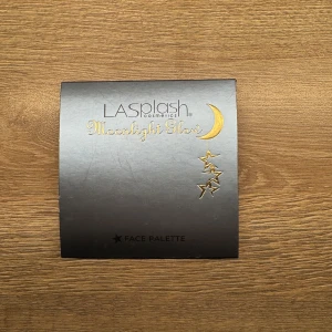 Moonlight Glow Face Palette från LA Splash - En sminkpalett med fyra olika puderprodukter: en orange rouge (Celestial Peach), en rosa rouge (Stellar Pink), ett brunt contourpuder (Twilight Contour) och ett vitt setting powder (Cloud 9 Setting Powder). Paletten har spegel och rymdtema.