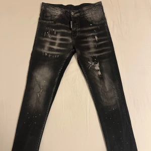 Svarta jeans från Dsquared2 - Snygga svarta jeans från Dsquared2 med coola slitningar och stänkdetaljer. De har en snygg logga på baksidan och en slim passform. Perfekt för att lägga till en unik touch till din outfit. Skulle säga att de passar som en 28-30W. Tveka inte på att höra av dig ifall du har några som helst frågor! 💯💪