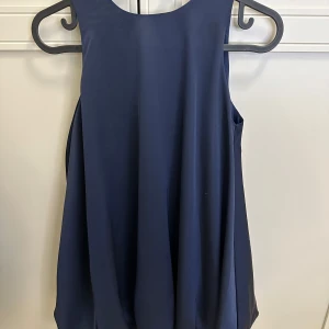 Barn Mörkblå ärmlös klänning med rosett. Köpt på Nk.  Konges slöjd.  - Elegant mörkblå ärmlös klänning med en stor vit rosett bak.  Köpt på nk. Märke :  Konges Slöjd. 