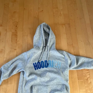 HOODRICH TRACKSUIT, PRIS KAN DISKUTERAS  - Snygga grå mjukisbyxor från Hoodrich med blå och vit logga på benet. Byxorna har en bekväm passform med resår och snörning i midjan samt muddar vid bensluten. Perfekta för en avslappnad stil.