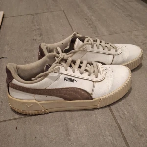 Vita och lila sneakers från Puma - Säljer ett par vita sneakers från Puma med lila detaljer. Skorna har snörning och en klassisk design med Pumas logga på sidan. Perfekta för en avslappnad stil. Dem är andvändna men jag har tvättat dem. Priset kan diskuteras 