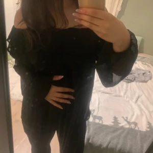Svart offshoulder blus - Snygg svart offshoulder blus med långa ärmar. Perfekt för en kväll ute eller en speciell tillställning. Blusen har en elegant och stilren design som framhäver axlarna.