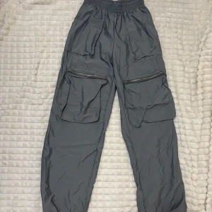 Grå cargopants med dragkedja - Snygga grå cargopants med flera praktiska fickor och dragkedjor. Byxorna har en loose passform och är perfekta för en avslappnad stil. Elastisk midja för extra komfort.