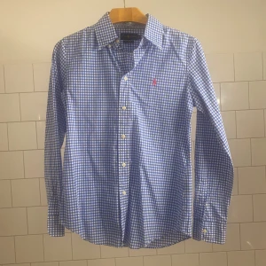 Ralph Lauren skjorta  - Snygg blå och vit rutig skjorta från Ralph Lauren med broderad logga i rött på bröstet. Skjortan har långa ärmar och knappar framtill. Perfekt för en stilren look! 10/10 skick mer eller mindre helt ny, storlek 8 skulle säga att den passar XS/S beroende på hur man vill att den ska sitta. Nypris 1700kr❌ Vårt pris 199✅