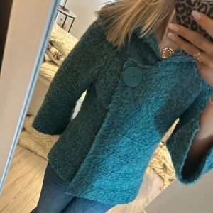 Stickad kofta med stor knapp - Säljer en mysig turkos stickad kofta med stor knapp framtill. Den har en unik textur och en härlig färg som verkligen sticker ut. Perfekt för att hålla sig varm och stilren.