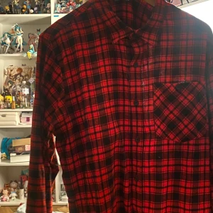 Röd och svart rutig skjorta - Den är i XL och har täcken på användning men inga tydliga defekter eller märken 