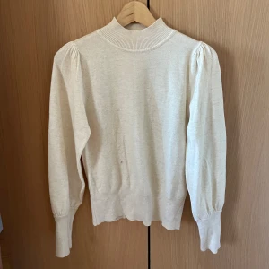 Beige polotröja - Säljer en stilren beige polotröja med långa ärmar och ribbade muddar. Perfekt för kyligare dagar och enkel att matcha med olika outfits.