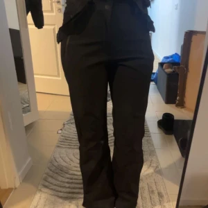 Svarta skidbyxor med hängslen - Snygga svarta skidbyxor med justerbara hängslen och dragkedja. Byxorna har rak form och ser helt helt oanvända ut. Använda endast en gång. Bilderna har inte super bra kvalite så skriv privat för tydligare bilder