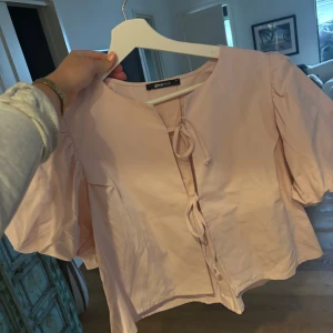 Rosa blus från Gina Tricot - Säljer en söt rosa blus från Gina Tricot med knytning framtill. Blusen har korta puffärmar och en rund halsringning🌸