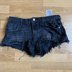 Svarta jeansshorts från Zara - Snygga svarta jeansshorts från Zara med slitna detaljer och fransig kant. De har en knapp och dragkedja framtill samt fem fickor. Mycket fint skick! Pris går att diskutera så hör av dig vid frågor