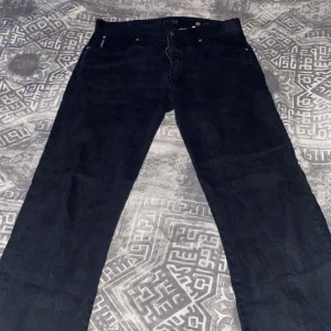 Armani Jeans - Snygga svarta jeansbyxor från Armani med klassisk femficksdesign. Byxorna har en diskret logga på bakfickan och en liten etikett vid framfickan. Perfekta för en stilren look.