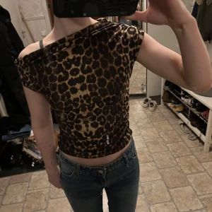 Leopardmönstrad offshoulder topp - Snygg leopardmönstrad offshoulder topp med rynkade detaljer. Perfekt för en trendig look. Toppen har en tight passform och är tillverkad i ett mjukt material som känns skönt mot huden.