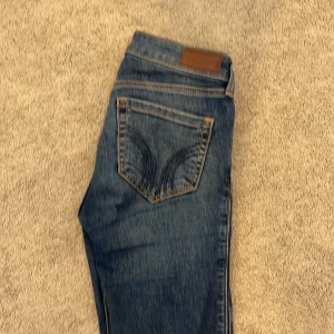 Blå jeans från Hollister - Snygga blå jeans från Hollister i modellen low-rise boot. De har en klassisk femficksdesign och är tillverkade i ett mjukt stretchmaterial för extra komfort. Perfekta för en avslappnad stil.