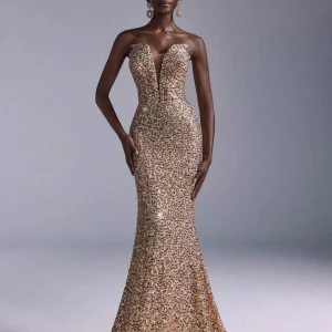 Balklänning- Glittrig guldklänning - Säljer en fantastisk glittrig guldklänning med djup v-ringning och figurnära passform. Klänningen är axelbandslös och har en elegant lång design som passar perfekt för speciella tillfällen. Den är täckt av paljetter som ger en lyxig känsla. Perfekt för att glänsa på festen!, helt oanvänd (nyskick) säljer då jag bestämde mig för en annan klänning💕