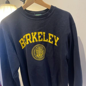 Mörkblå vintage college sweatshirt från Champion med Berkeley-tryck. Nypris 699. - Säljer en sweatshirt från Champion med gult Berkeley-tryck på framsidan. Tröjan är tillverkad i fleece och har långa ärmar. Perfekt för en avslappnad stil.