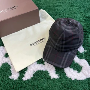  Burberry keps  - Snygg rutig keps från Burberry i mörka nyanser. Kepsen har en klassisk design med en justerbar rem baktill för perfekt passform. Perfekt för att ge din outfit en stilfull touch. OBS UTAN KVITTO OCH UTAN BOX
