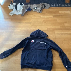 Marin blå hoodie från Champion - Säljer en svart hoodie från Champion med broderad logga på bröstet. Den har en klassisk design med känguruficka och långa ärmar. Perfekt för en avslappnad stil.