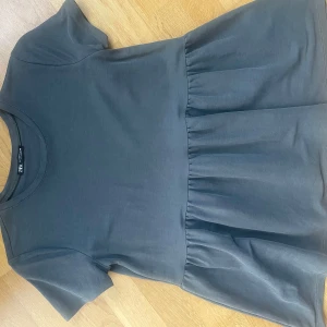 Grå topp från Zara - Säljer en gullig mörkgrå topp från Zara med korta ärmar och en volangdetalj nedtill. Storlek S, men lite större i modellen. Inga defekter. Hör av dig vid frågor! 💗