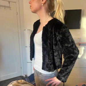 Svart pälsjacka  - Säljer en snygg svart pälsjacka. Jackan är kort och har en mjuk, fluffig yta som ger en lyxig känsla. Perfekt för att höja din outfit till nästa nivå. Den har långa ärmar och en öppen design utan knappar eller dragkedja.