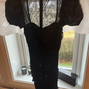 Svart klänning från Missguided - Snygg svart klänning från Missguided med kort puffärm och transparenta detaljer. Klänningen har en dragkedja bak och en figurnära passform. Perfekt för en kväll ute eller en speciell tillställning.