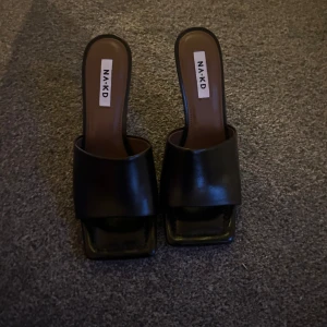 Svarta klackskor från NA-KD - Snygga svarta klackskor från NA-KD med öppen tå och fyrkantig form. Skorna har en elegant design med en smal klack som ger en stilren look. Perfekta för att lyfta din outfit till nästa nivå.