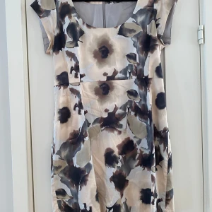 Blommig klänning från Tiger of Sweden - Säljer en elegant blommig klänning från Tiger of Sweden. Klänningen har korta ärmar och ett vackert mönster i beige, svart och grå toner. Perfekt för en stilfull look. Ny brun och beige klänning i strl 42 från Tiger of Sweden, modell Tiara prnt.  Klänningen har en underklänning.  Ny, aldrig använd.  Mått Över bröstet: ca 51 cm Längd från axeln och ner: ca 86 cm  94% bomull och 6% elastan, underklänning 100% viskos.  Kommer från ett djur och rökfritt hem. 