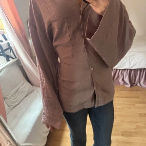 Brun skjorta från H&M - Snygg brun skjorta från H&M med en avslappnad passform. Skjortan har långa ärmar och knappar. Oversized ärmar