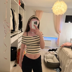 Randig offshoulder topp - Snygg offshoulder topp med svart och beige randigt mönster. Perfekt för en stilren look. Passar bra till både jeans och kjol.