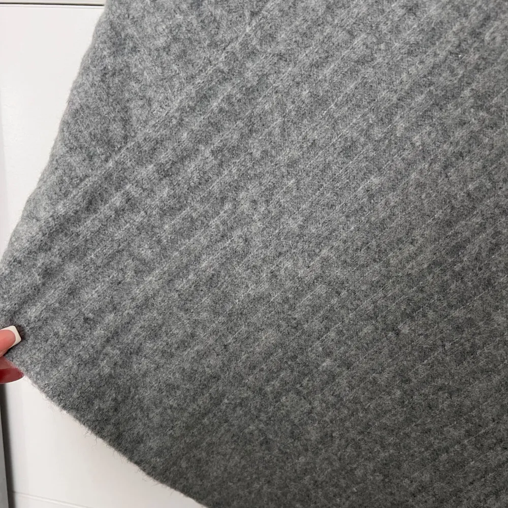 Säljer en stilren grå stickad poncho med v-ringning. Perfekt för kyliga dagar och ger en mysig känsla. Den har en enkel design med ett diskret mönster som ger textur.. Neuletakit & Villapaidat.