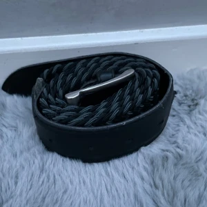 Bälte - Bältet är 104cm långt. Det är svart med ljuse gråa detaljer. Det är and syt 