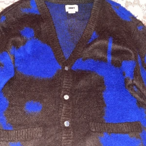 Brun och blå kofta från Obey - Säljer en unik brun och blå kofta från Obey med ett abstrakt mönster. Koftan har knappar framtill och två fickor. Perfekt för att ge din outfit en cool touch.Köpte den för 700kr och använder den knappas. Vill sälja den för 500kr.