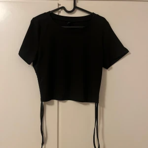 Svart kortärmad topp med knytband - Säljer en stilren svart topp med korta ärmar och knytband i sidorna. Perfekt för en trendig look. Passar bra till både jeans och kjol.