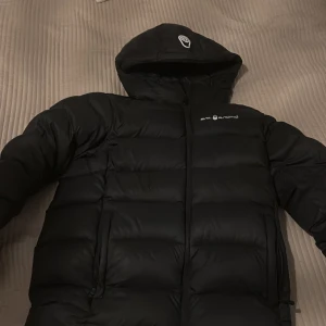 Svart dunjacka från Peak Performance - Säljer en svart dunjacka från Peak Performance. Jackan har en dragkedja framtill och är långärmad med en huva. Perfekt för kalla dagar.