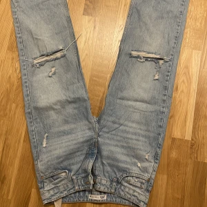 Ljusa jeans med slitningar från Zara - Jag säljer ett par ljusblå jeans från Zara. De har typ inte använts så mycket och är nästan som nya. De är tighta vid midjan och sitter bra på kroppen. De är midrise och har slitningar för en cool look. Priset kan vi snacka om om du är intresserad