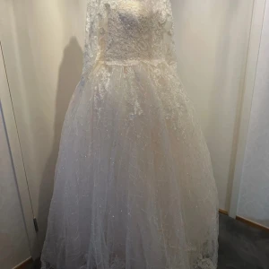 Vit spetsklänning med pärlor - Elegant långklänning i vit spets med detaljerade pärlor och broderier. Klänningen har en vacker struktur och ger en lyxig känsla. Perfekt för speciella tillfällen.