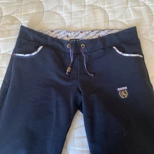 Svarta mjukisbyxor från Tommy Hilfiger - Snygga svarta låg midjade mjukisbyxor från Tommy Hilfiger med dragsko i midjan och broderad logga på benet. Byxorna har fickor med mönstrad kant och en bekväm passform. Perfekta för en avslappnad stil. Storlek M på byxor men dom e som S 