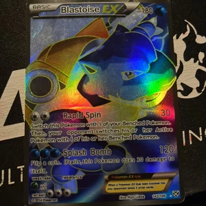 Blastoise EX Pokémonkort - Säljer ett Blastoise EX Pokémonkort med holografisk yta. Kortet har 180 HP och attacker som Rapid Spin och Splash Bomb. Perfekt för samlare eller spelare som vill förstärka sin kortlek. Kortet är från 2014 och illustrerat av Ryo Ueda.