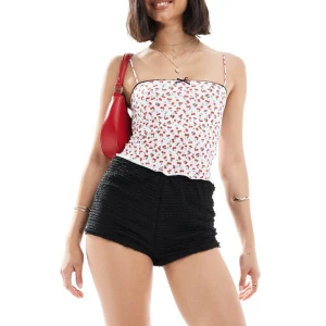 Linne med körsbärsprint - Säljer en söt vit linne från Bershka med ett färgglatt körsbärsmönster. Toppen har smala axelband och en liten svart rosett framtill. Perfekt för sommardagar! 🍒