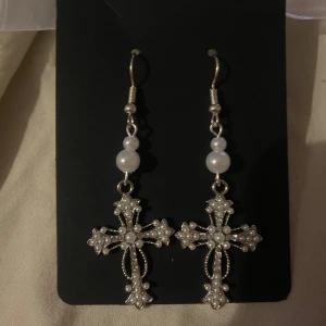 Silvriga korsörhängen med pärlor - Egengjorda örhängen i form av kors, dekorerade med små vita pärlor. De har en krok för enkel användning och en klassisk design som passar perfekt för speciella tillfällen.