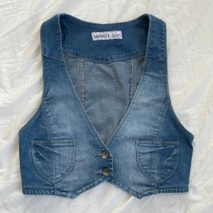 Jeansväst y2k - Snygg y2k jeansväst från Monica's Jeans i en klassisk blå denimfärg. Västen har en v-ringad design med två knappar framtill och praktiska fickor. Ger nostalgi till Hannah Montana stil✨